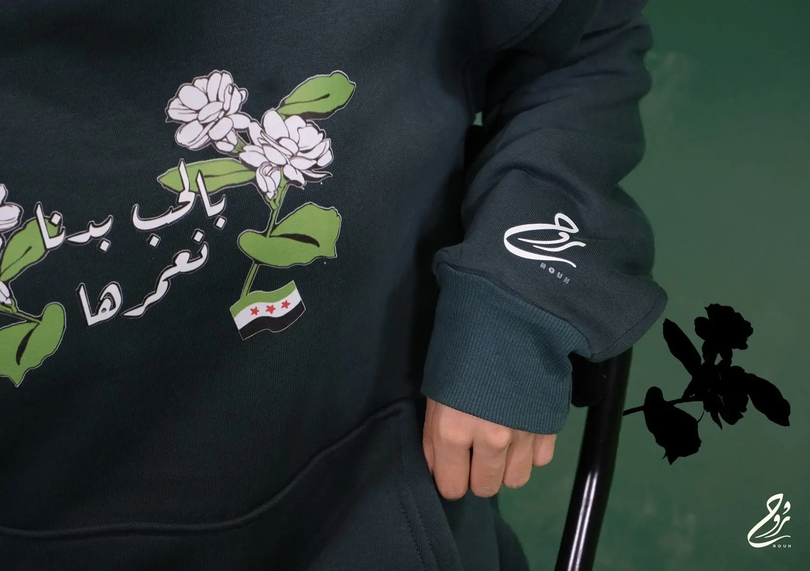 . العبارة بخط عربي مزخرف إلى جانب زهرة الياسمين السورية الشهيرة، في إشارة إلى الكلمات الغنائية المحبوبة في سوريا ُكتبت
يهدف التصميم إلى تذكيرنا بروح الأمة السورية التي تتحدى كل الصعاب من أجل استعادة سوريا التي نحبها